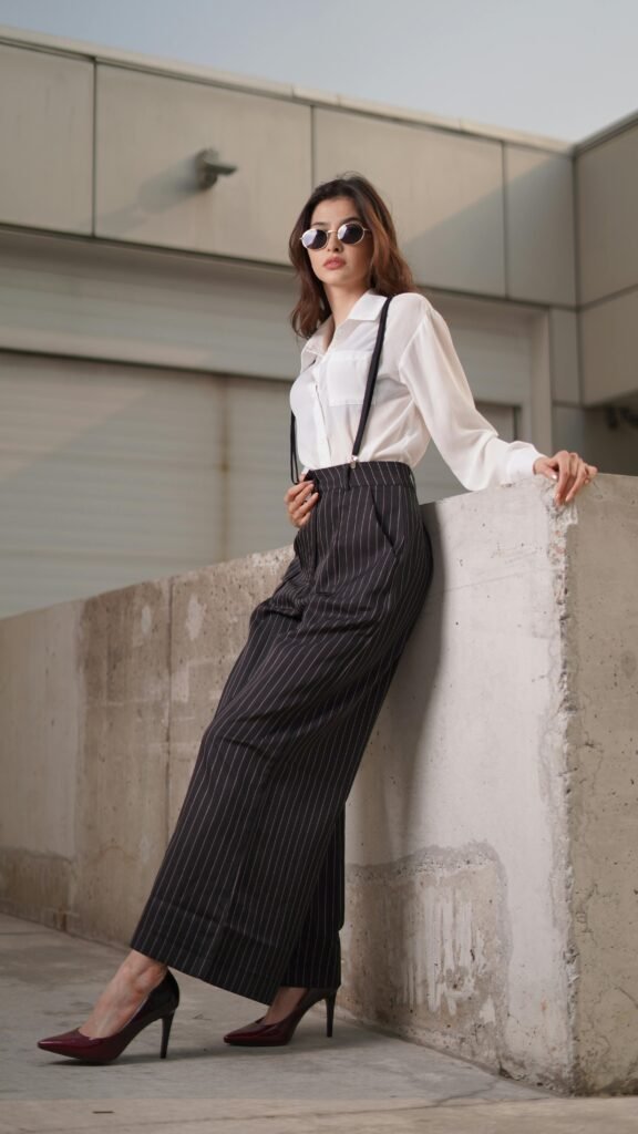 A fashionable woman poses outdoors in a chic white blouse and pinstriped pants, exuding confidence and style.